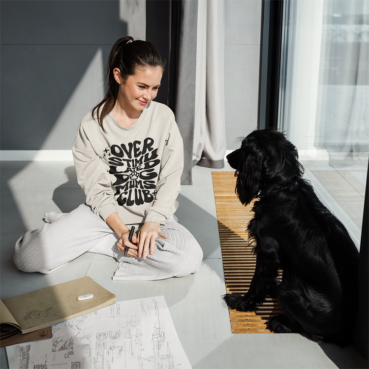 female sitting on the floor in the sun wearing her overstimulated dog mums crew looking at her black dog